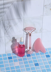 Serum bottle and jade massage roller, scraper gua sha on tile with palm leaf shadow. Creative...
