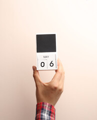 Date May 6, block calendar in male hand on beige background
