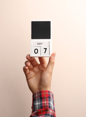 Date May 7, block calendar in male hand on beige background