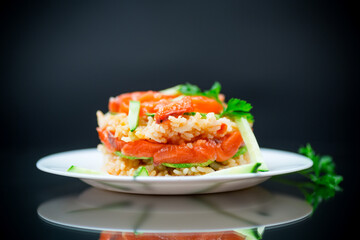 Boiled white rice with salted red fish, cucumbers and other vegetables with herbs in a plate.