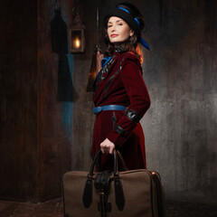 A stylish lady in a burgundy old-fashioned suit with a hat and a valise. Brunette in a retro style suit