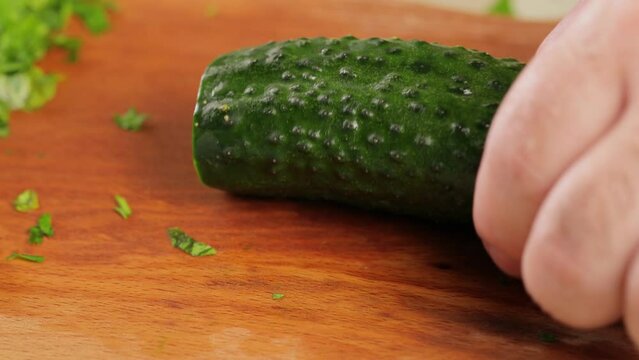 Preparing cucumber for chopping, cutting it lengthwise in half on wooden cutting board. Close-up
