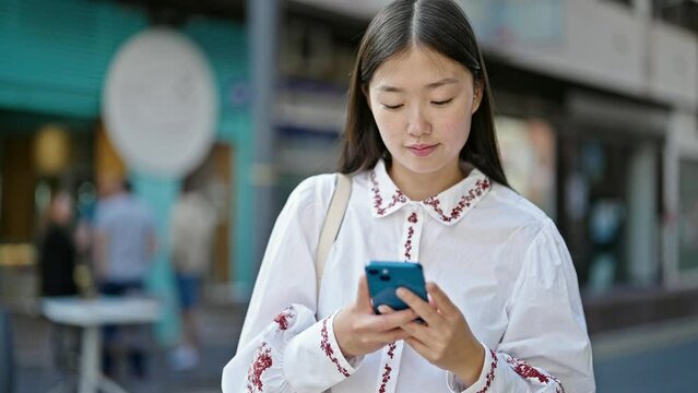 Young chinese woman using smartphone smiling at street