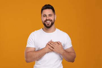 Thank you gesture. Happy grateful man holding hands near heart on orange background