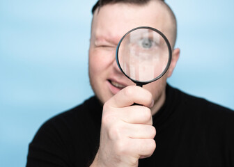 Squinting while reading the text through a magnifying glass, a young handsome man has poor...