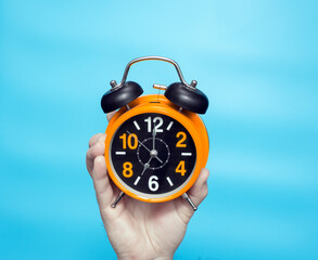 Clock time concept. Alarm clock in a man's hand on a blue background on the clock hands 7 in the...