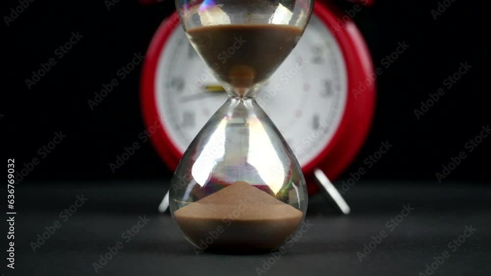 Poster timelapse of an hourglass with an alarm clock on the blurred background - concept of time