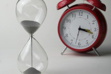 Glass hourglass and an old-fashioned alarm clock depicting the passage of time