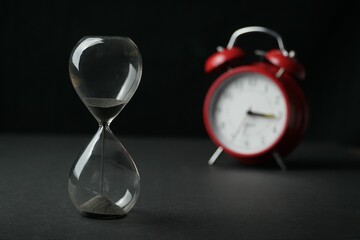 Glass hourglass and an old-fashioned alarm clock depicting the passage of time