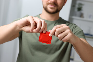 Closeup view of man opening pack with condom indoors