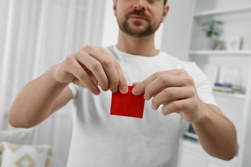 Closeup of man opening pack with condom indoors