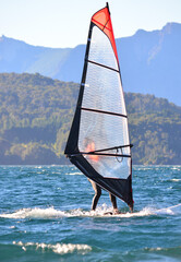 windsurfing on a lake. windsurfer going upwind doing water sports with mountains in the background