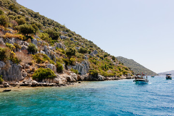 Fototapeta premium Beautiful view of the Mediterranean Sea with yachts. Picturesque landscape of blue ocean and green mountains on a sunny summer day. The sunken city of Kekova, Türkiye - 28 July 2023