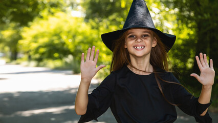 Young kid dressed up for Halloween festival. Portrait little girl in a witch costume, outside.