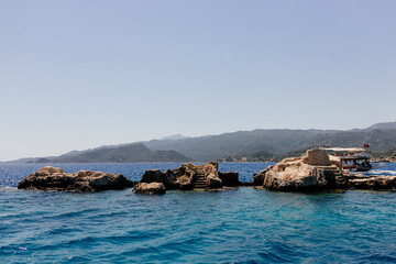 Fototapeta premium Beautiful view of the Mediterranean Sea with yachts. Picturesque landscape of blue ocean and green mountains on a sunny summer day. The sunken city of Kekova, Türkiye - 28 July 2023