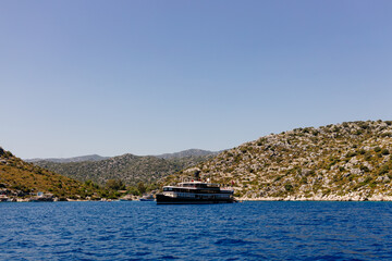 Fototapeta premium Beautiful view of the Mediterranean Sea with yachts. Picturesque landscape of blue ocean and green mountains on a sunny summer day. The sunken city of Kekova, Türkiye - 28 July 2023
