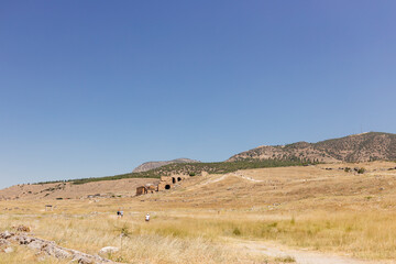Half-ruined buildings of the ancient city, Journey to the old city. Preserved old columns against the backdrop of a mountain landscape. Hierapolis Ancient City, Pamukkale, Türkiye - July 29, 2023