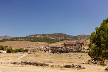 Half-ruined buildings of the ancient city, Journey to the old city. Preserved old columns against the backdrop of a mountain landscape. Hierapolis Ancient City, Pamukkale, Türkiye - July 29, 2023