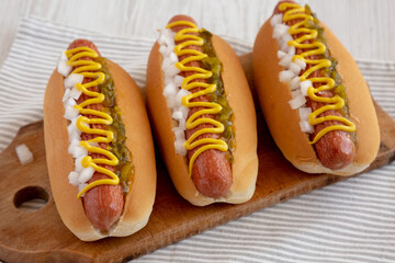 Char Grilled Hot Dog with Mustard, Relish and Onion on a rustic wooden board, side view.
