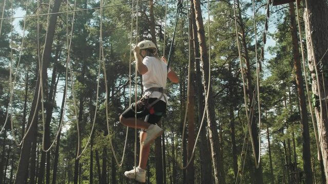 Brave teenage girl in gear, passing an obstacle course in a rope town in a wooded area. Steadicam shot