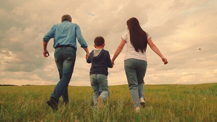 Happy family runs in park on green grass. Family game, teamwork. Dad mom child son run in nature. Mom dad, child play hand in hand outdoors. Healthy lifestyle father mother child. Child son, parents