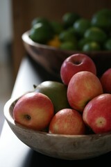 Wooden table displays a bowl of assorted fresh fruits including apples, and limes