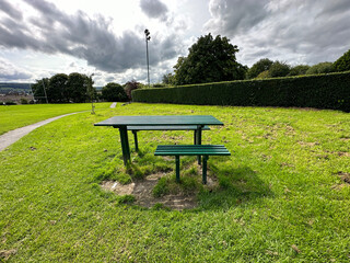 A green table, and benches, set in the green space of, Silsden Playing Fields, on a cloudy day in Silsden, UK