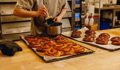 Baker brushes glaze onto freshly baked golden pastries in professional kitchen