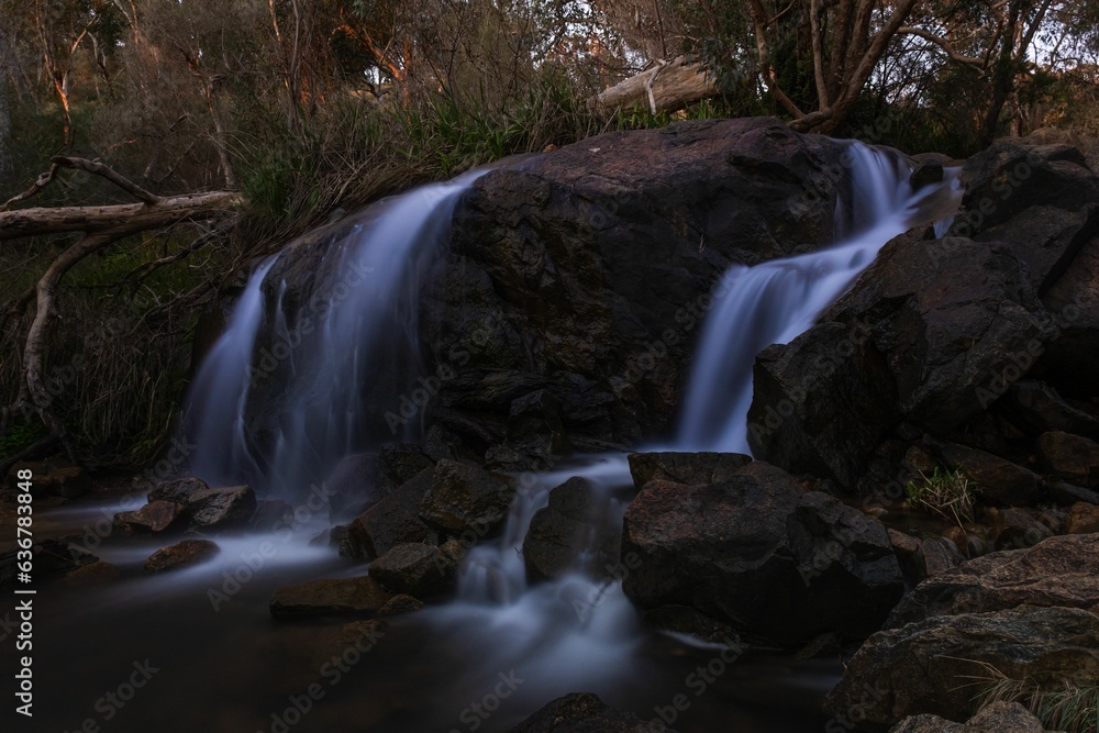 Poster long exposure shot of a tranquil waterfall cascading down the rocks in a lush forest of trees