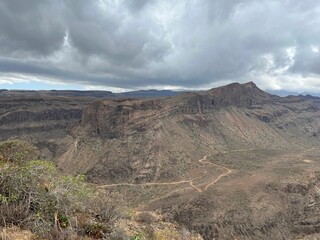 Vast valley surrounded by towering rocky mountain peaks, with wispy clouds above