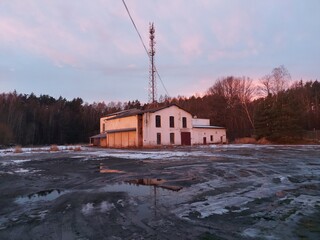 Opuszczona hala przemysłowa z masztem telefonicznym przy lesie zimą