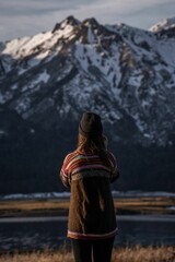 Vertical shot of a young woman standing on the background of the snowy mountain in the highland