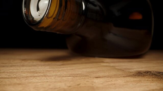 I place the empty black whiskey bottle on the table, and the last drops are dripping from it onto the wooden surface, macro slider.