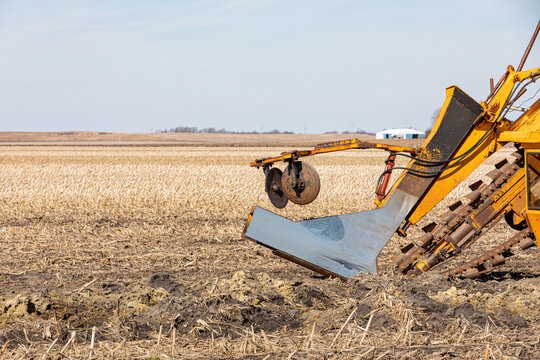 Field tile plow machine in farm field. Water drainage, soil conservation and agriculture flooding control concept