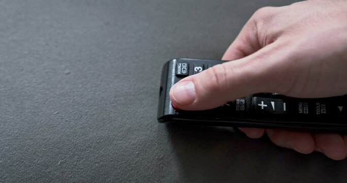 A man turns on the TV with his thumb using a black TV remote control.