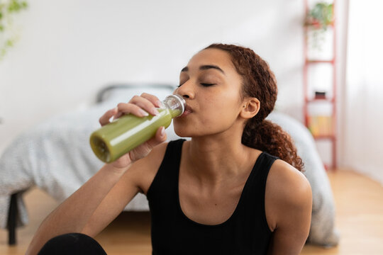 Young Latin Woman Drinking Detox Green Juice After Workout Routine At Home. Healthy Lifestyle Concept