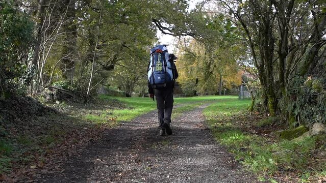 Randonneur avec un gros sac &agrave; dos qui marche de dos dans un chemin
