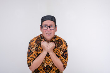 An alarmed southeast asian muslim man clenching his collar in fear. Wearing a batik shirt and...