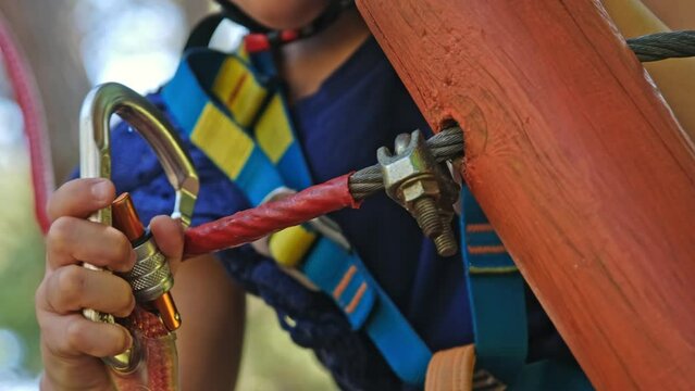 Caucasian Child Girl Attaching Double Spring Loaded Carabiner Snap Hook to Metal Safety Cable Line in Rope Park Obstacle Course