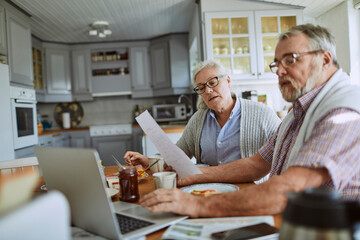 Senior couple going over their bills and home finances while having breakfast in the morning