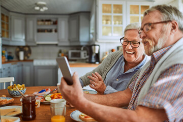 Senior couple having breakfast together at home and using a smart phone