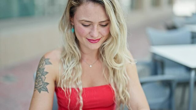 Young blonde woman using laptop sitting on table at coffee shop terrace