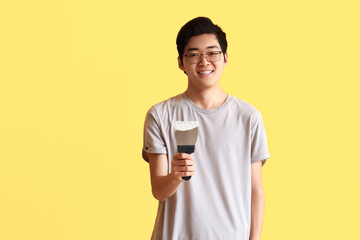 Young Asian man with putty knife on yellow background