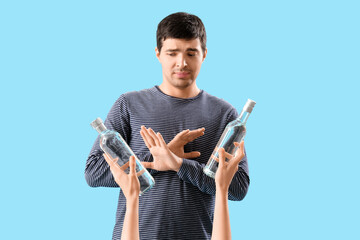 Young man rejecting bottles of vodka on blue background