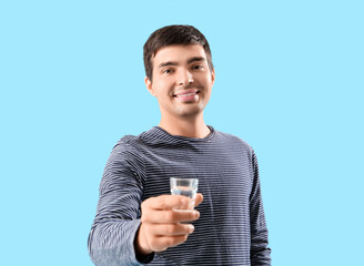 Young man with glass of vodka on blue background