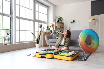 Young woman with wooden airplane unpacking suitcase at home