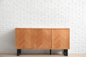 Stylish wooden chest of drawers near light brick wall