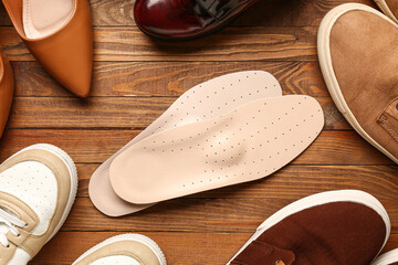 Pair of leather orthopedic insoles and different shoes on wooden background, closeup - obrazy, fototapety, plakaty