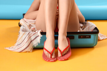 Female legs in stylish flip flops with suitcase on yellow background - obrazy, fototapety, plakaty