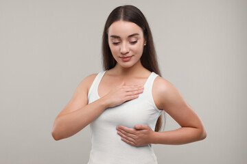 Beautiful young woman doing breast self-examination on light grey background